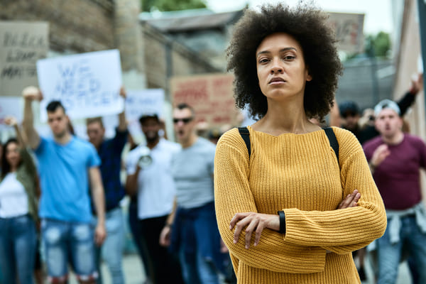 Mulher confiante de braços cruzados em frente a uma manifestação pública.