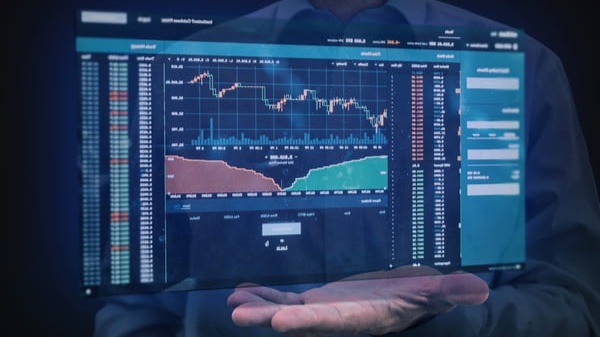 Tela de análise de mercado financeiro com gráficos de ações e indicadores econômicos projetada sobre a mão de um investidor.