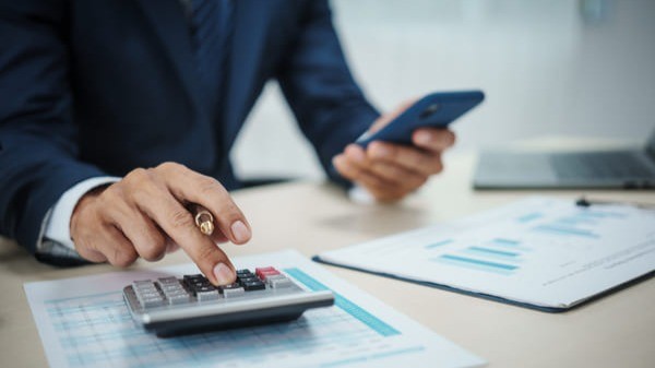 Pessoa usando calculadora e celular em mesa de escritório com documentos financeiros, representando cálculos atuariais e gestão de RPPS.