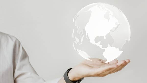 Pessoa segurando projeção holográfica de um globo terrestre, simbolizando o cenário econômico global e as perspectivas econômicas internacionais.