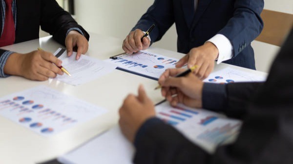 Pessoas em reunião analisando gráficos financeiros e discutindo estratégias de investimentos e gestão atuarial para regimes próprios de previdência.