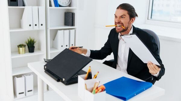 Homem estressado em escritório segurando documentos e mordendo um lápis, representando o impacto das emoções nas decisões financeiras e nos investimentos.