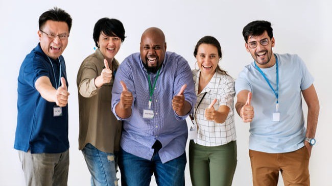 Grupo diverso de cinco pessoas sorrindo e fazendo sinal de positivo, simbolizando conquista, motivação e sucesso, em ambiente claro e amigável.